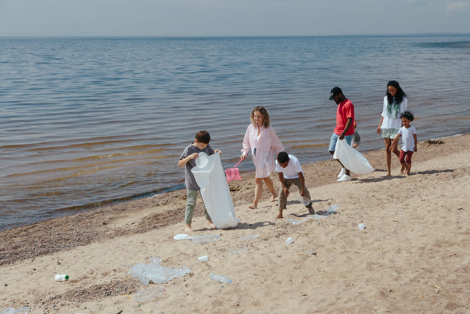 Un grupo de adultos y niños recoge plástico en la orilla del mar